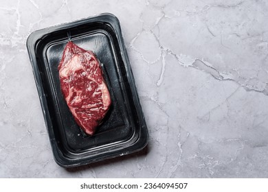 Fresh raw beef ribeye steak sealed in a vacuum pack, preserving its quality and freshness. Flat lay with copy space - Shutterstock ID 2364094507