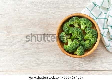 Fresh raw broccoli florets in a wooden bowl on a white cuisine table, top view.