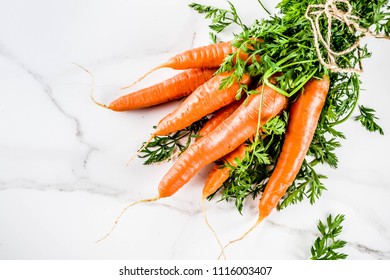 Fresh raw carrots with green leaves, white marble background copy space top view