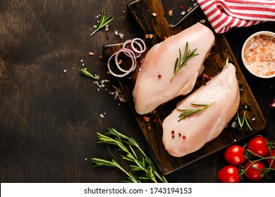 Fresh raw chicken meat fillet with salt, pepper, onion and butter on a wooden board on a dark wooden rustic background. Top view.