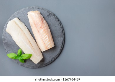 Fresh raw cod fillet with basil on a stone plate, horizontal, copy space, top view