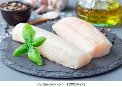Fresh raw cod fillet with spices, pepper, salt, basil on a stone plate, horizontal