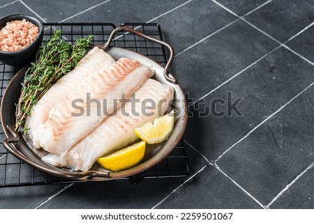 Fresh raw cod fish fillets with herbs served on steel tray. Black background. Top view. Copy space.