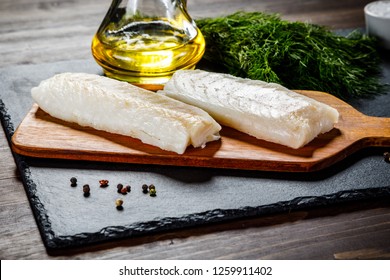 Fresh Raw Cod With Herbs Served On Black Stone On Wooden Table