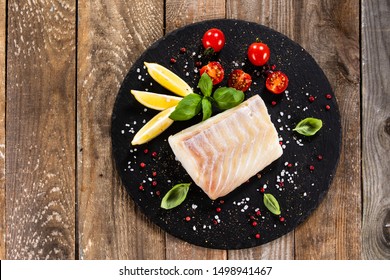 Fresh Raw Cod With Herbs Served On Black Stone On Wooden Table