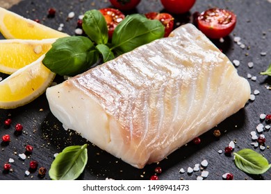 Fresh Raw Cod With Herbs Served On Black Stone On Wooden Table