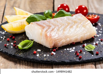 Fresh Raw Cod With Herbs Served On Black Stone On Wooden Table