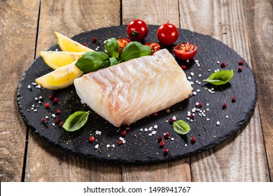 Fresh Raw Cod With Herbs Served On Black Stone On Wooden Table