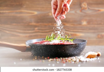 Fresh raw flank steak in the pan. The woman's hand adds salt to the meat. Ingredients are spices, rosemirine various sprouts and finally salt. - Powered by Shutterstock