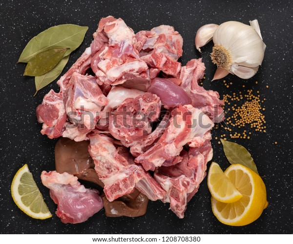 Fresh raw\
goat meat stew like cuts on black cutting board with spices\
(mustard seeds, garlic, lemon, and bay\
leaves).
