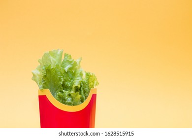 Fresh Raw Green Lettuce Leaves In A Package From Red French Fries On A Yellow Background Copy Space, One Leaf Lies Nearby, Proper Nutrition, Healthy Lifestyle Concept, Replacing Unhealthy Food