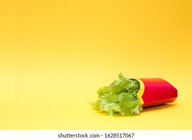 Fresh Raw Green Lettuce Leaves In A Package Of Red French Fries On A Yellow Background Copy Space, One Leaf Lies Nearby,  Healthy Lifestyle Concept, Contrast Between Healthy And Unhealthy Food