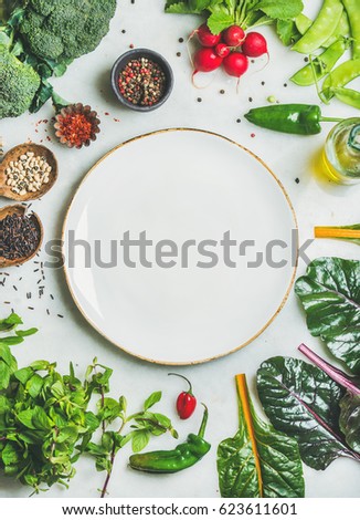 Fresh raw greens, unprocessed vegetables and grains over light grey marble kitchen countertop, wtite plate in center, top view, copy space. Healthy, clean eating, vegan, detox, dieting food concept