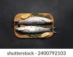 Fresh raw grey mullet fish on the cutting board with spices and herbs on black stone table top view. Healthy food concept.