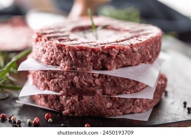 Fresh raw ground beef patties with rosemary salt and pepper made in a meat form on a cutting board. - Powered by Shutterstock