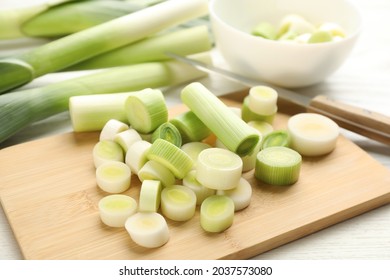 Fresh raw leek slices and knife on white wooden table, closeup