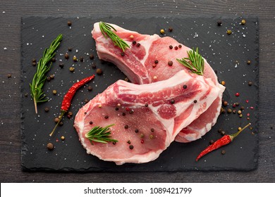 свежее сырое мясо со специями и розмарином и красным перцем на черном сланце, на темном фоне, свинина, говядина, отбивная на кости