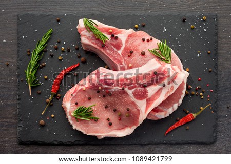 fresh raw meat with spices and rosemary and red pepper on black slate, on dark background, pork, beef, chop on a bone