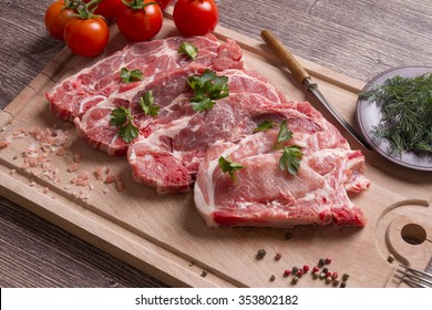 Fresh raw pork chop meat on cutting board with tomatoes, parsley and black pepper - Powered by Shutterstock