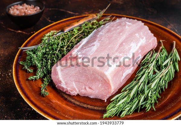 Fresh Raw pork loin meat with thyme\
and rosemary on rustic plate. Dark background. Top\
view