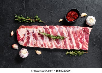 Fresh raw pork ribs with rosemary and garlic. Black background. Top view