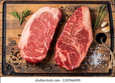 Fresh Raw Prime Black Angus Beef Steaks With Spices On Wooden Board: Striploin, Rib Eye. Top View. On A Dark Background