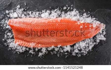 Fresh raw salmon fish steak on ice over dark stone background. Creative layout made of fish, top view, flat lay
