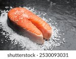 Fresh raw salmon steak with salt on dark textured table, closeup