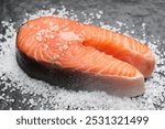 Fresh raw salmon steak with salt on dark textured table, closeup