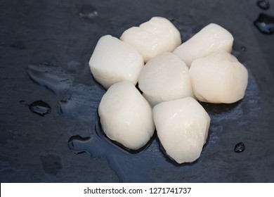 Fresh Raw Sea Scallops On Black Stone Plate. Lot Of Delicious And Tasty Scallop On Black Background With Water Drops.