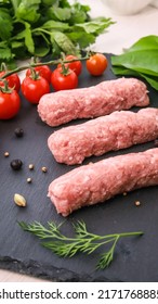 Fresh raw skewers or cevapi, Bosnian and Serbian traditional oriental dish of minced pork and lamb meat with fresh greens and tomatoes on black stone background 
