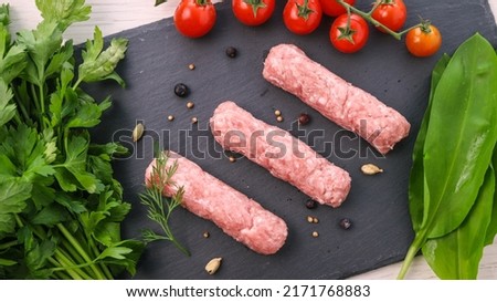 Fresh raw skewers or cevapi, Bosnian and Serbian traditional oriental dish of minced pork and lamb meat with fresh greens and tomatoes on black stone background 
