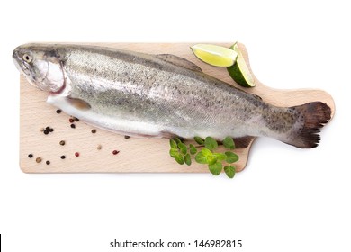Fresh raw trout with pepper and fresh herbs on wooden cutting board isolated on white background, top view. Culinary seafood eating.