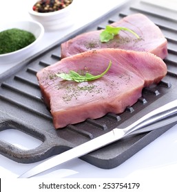 Fresh Raw Tuna Fish Fillet Steaks Ready For Cooking On A Cast Iron Griddle With Rocket Garnish, Mixed Herbs, Dill, Whole Mixed Pepper Corns And Filleting Knife On White Background Isolated