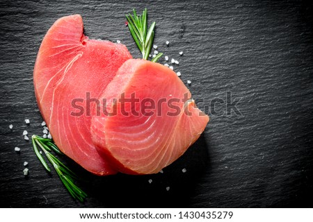 Fresh raw tuna steak with rosemary. On black rustic background