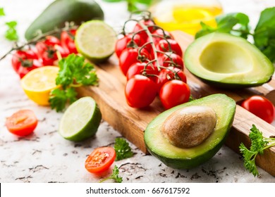 Fresh raw vegetable ingredients for healthy cooking. Avocado, cherry tomatoes, citrus and fresh herbs on wooden cutting board and table - Powered by Shutterstock