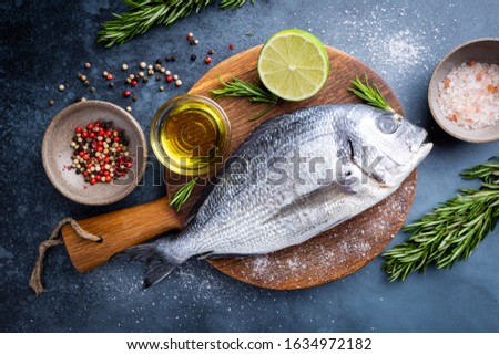 Fresh ready to cook raw bream fish dorado with ingredients and seasonings like rosemary, salt, pepper, lime and olive oil, top view