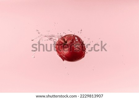 Fresh red apple on pink background with water splash