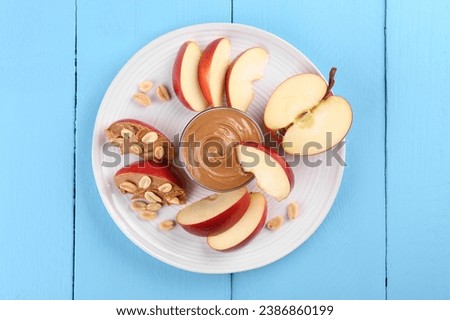 Fresh red apple with peanut butter and nuts on light blue wooden table, top view
