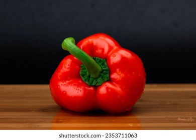 Fresh red bell pepper with water drops a wooden cutting board on a black background. - Powered by Shutterstock