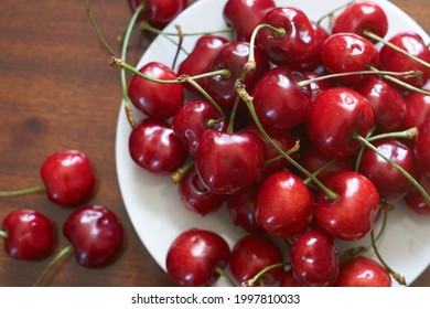 Fresh red cherries fruit on plate on wooden background close up. High quality photo - Shutterstock ID 1997810033