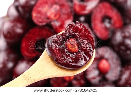 Fresh red cherry balanced on wooden spoon with blurred cherry background. Vibrant fruit image showcasing natural beauty and quality produce.