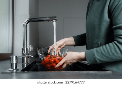 Fresh red Cherry tomatoes in bowl under water stream in sink, woman with no face in the kitchen washing vegetables before cooking, healthy eating - Powered by Shutterstock