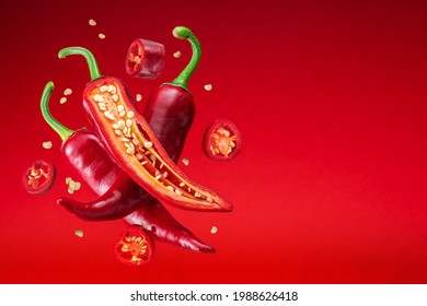 Fresh red chilli peppers and cross sections of chilli pepper with seeds floating in the air.