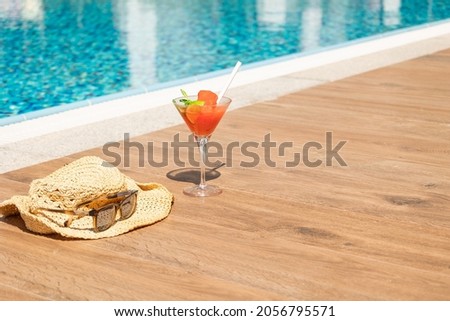 Fresh red cocktail with ice in glass, beach hat and sunglasses on swimming pool. Tropical juice on luxury vacations. Concept summer holiday and travel. High quality photo
