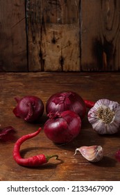 Fresh Red Onions, Garlic, Hot Chilli Pepper On Wooden Brown Kitchen Table. Seasonings, Spices, Flavourings On Rustic Country Background. Vertical Shot