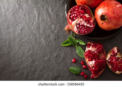 Fresh Red Pomegranate And Seed  With Leaves Over Black Stone Background , Overhead Or Top View