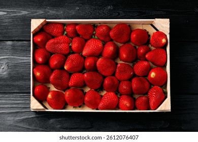 Fresh red strawberries in wooden box. Strawberry fruits on dark wooden table top view.