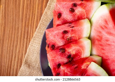 Fresh red watermelon pieces on a black plate on a wooden table. Sweet and juicy watermelon.