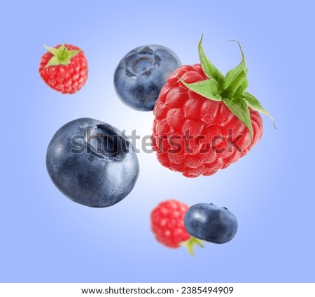 Fresh ripe blueberries and raspberries falling on pastel blue background